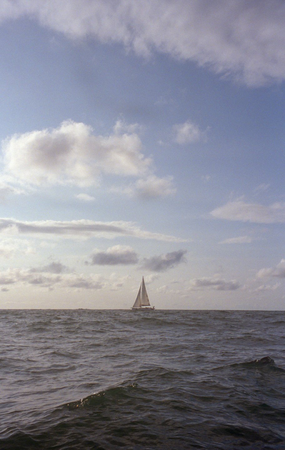 Sailboat on the open ocean under a partly cloudy sky.
