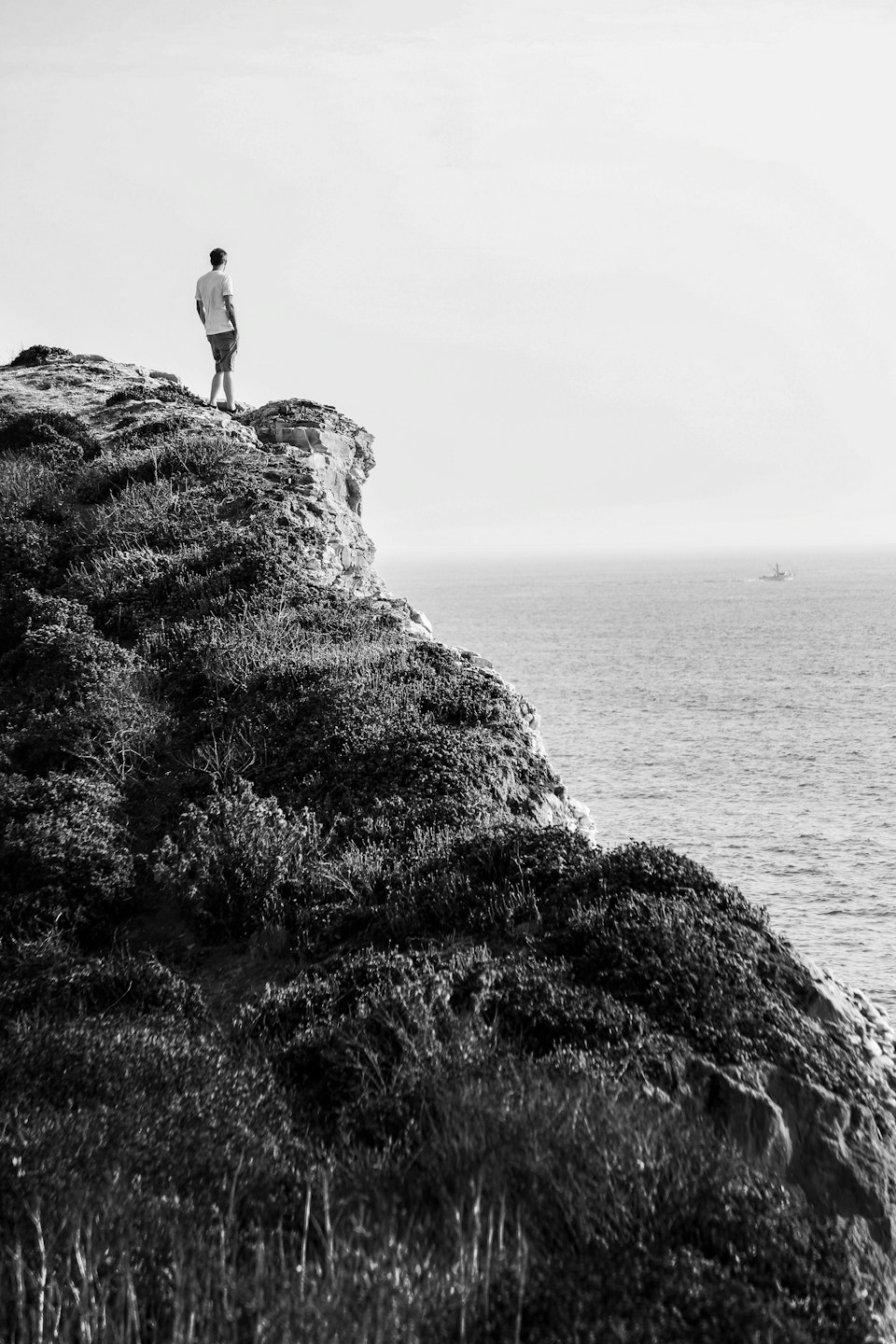 Man standing on a cliff edge overlooking the ocean.