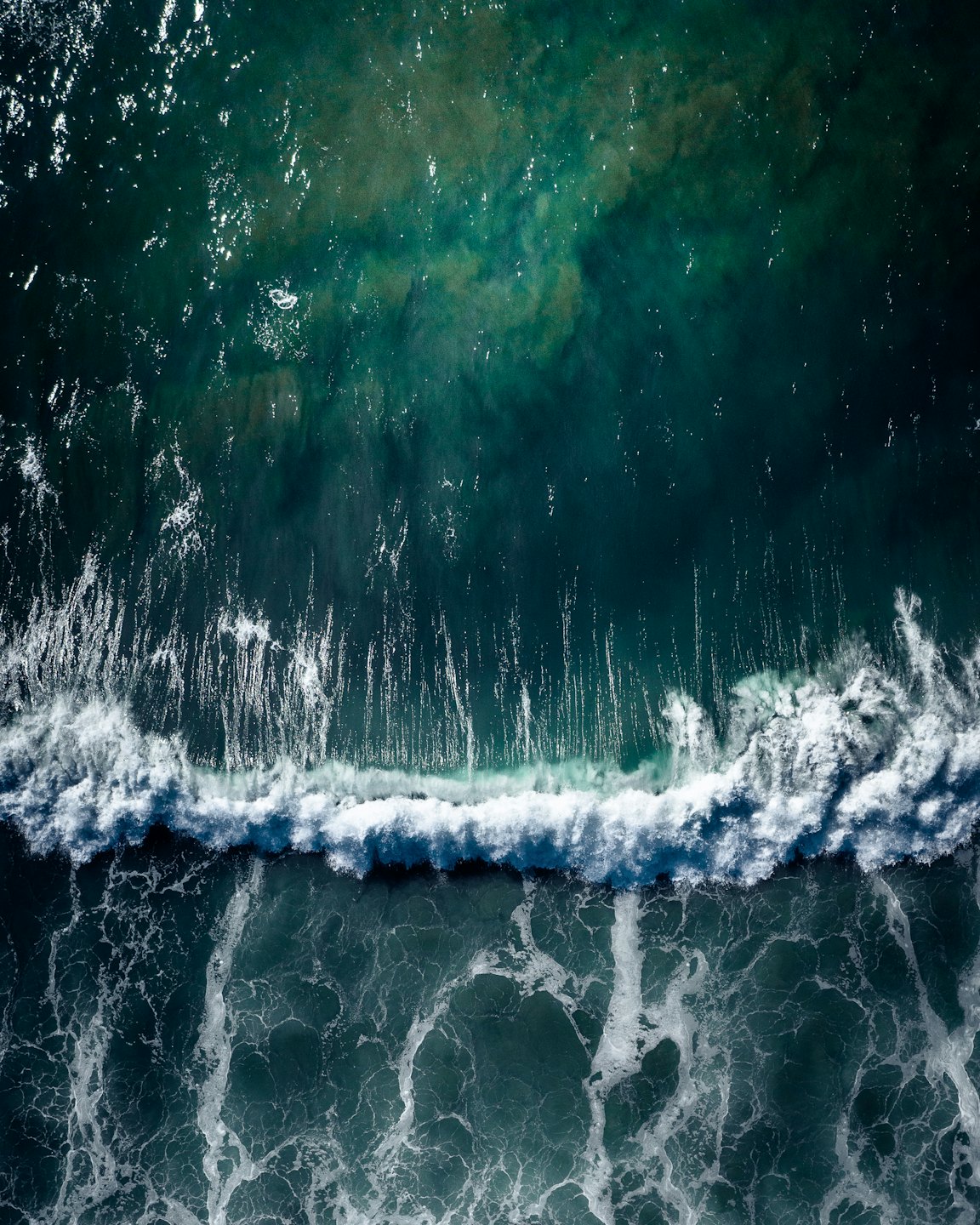 Ocean wave breaking with white foam on dark blue water.
