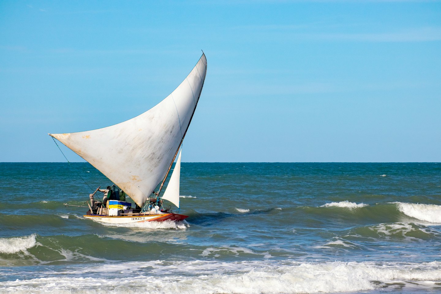 Sailboat with triangular sail on choppy ocean waves.
