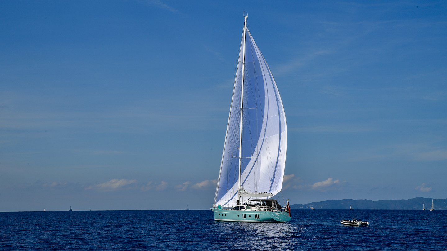 Sailboat with light blue hull sails the ocean.