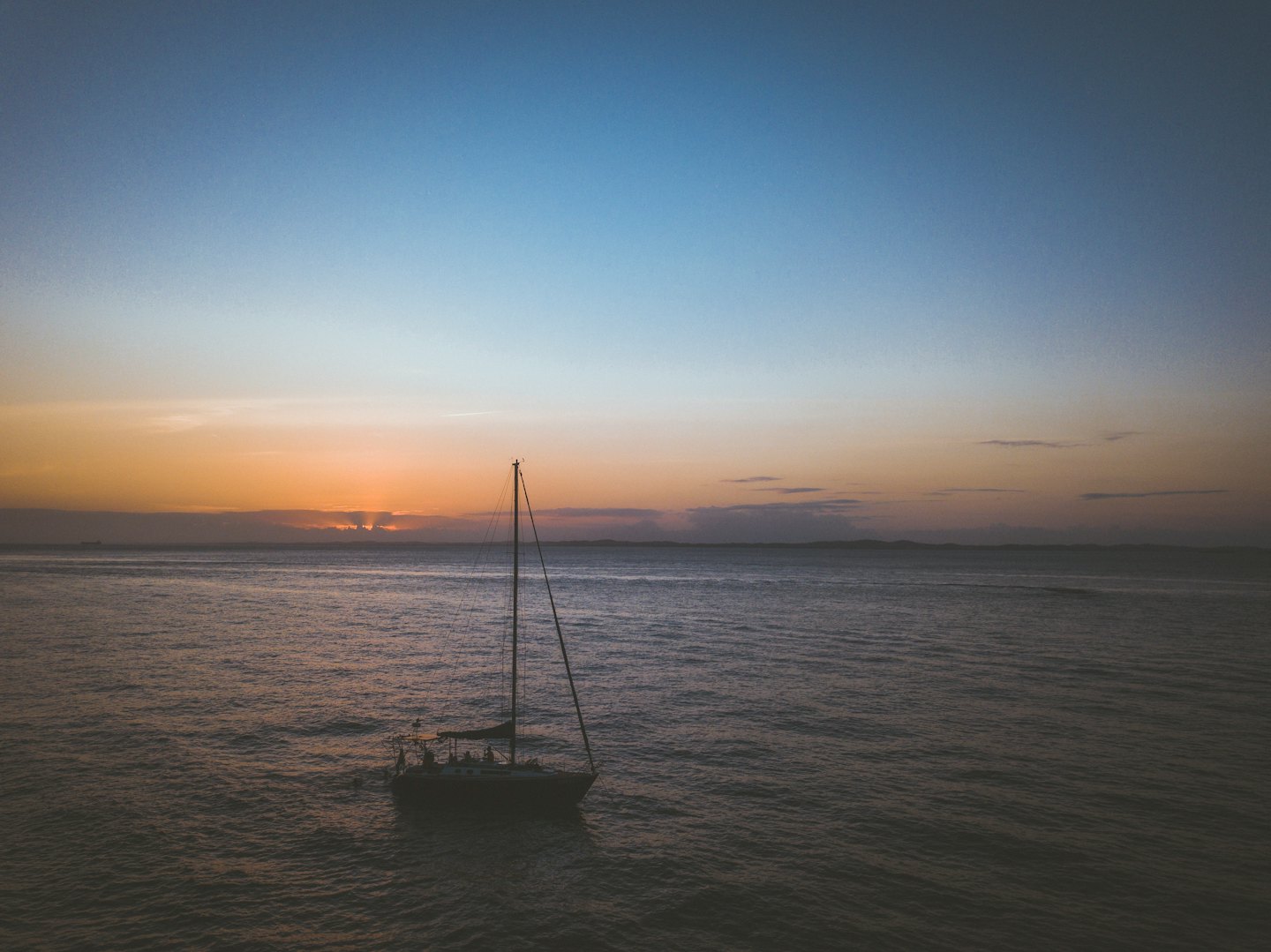 A lone sailboat crosses the ocean at sunset.